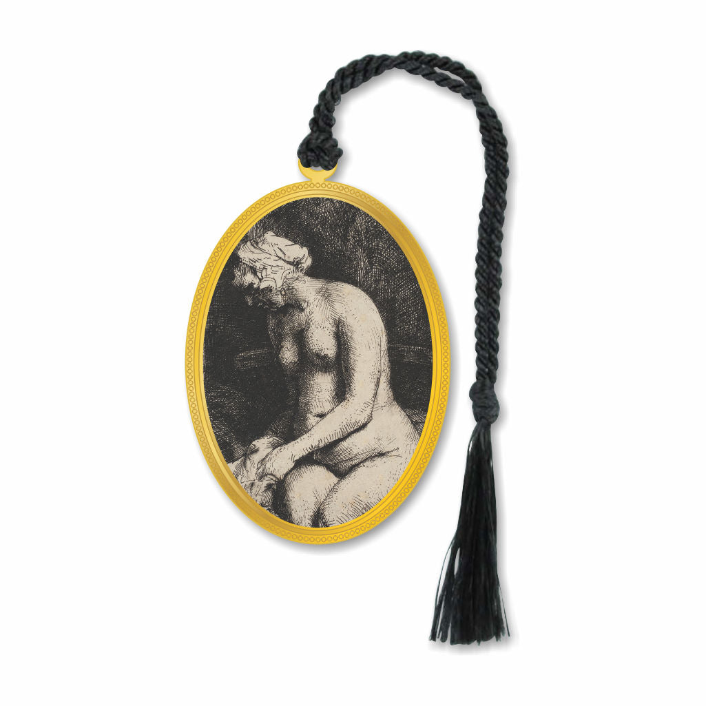 A metal bookmark featuring an etching of a nude woman by Rembrandt, surrounded by a gold oval border, with a black decorative tassel.