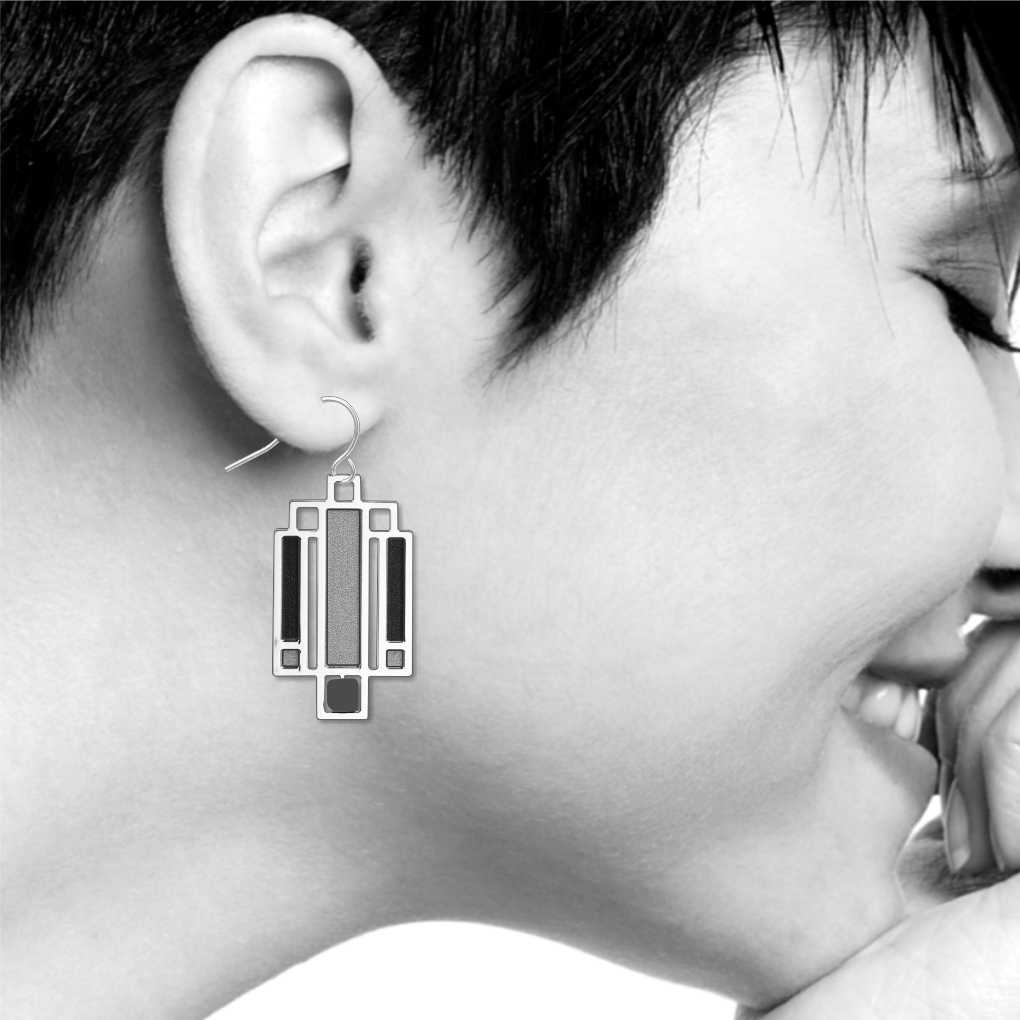 Willits Lightscreen Earrings: silver-tone geometric earring inspired by Frank Lloyd Wright's Willits House lightscreen design, featuring black, charcoal gray, and textured silver accents in a stained-glass-inspired architectural pattern shown on model