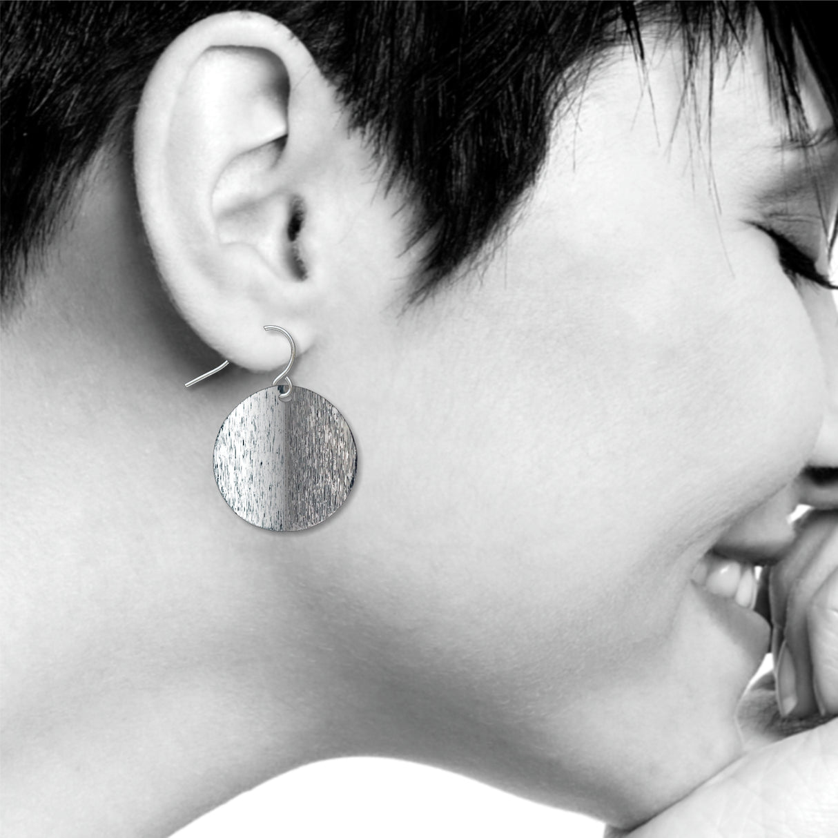 An Orb circular drop earring with a split-tone brushed silver finish, shown worn on ear with a sleek minimalist design inspired by Ellsworth Kelly’s sculptural artwork
