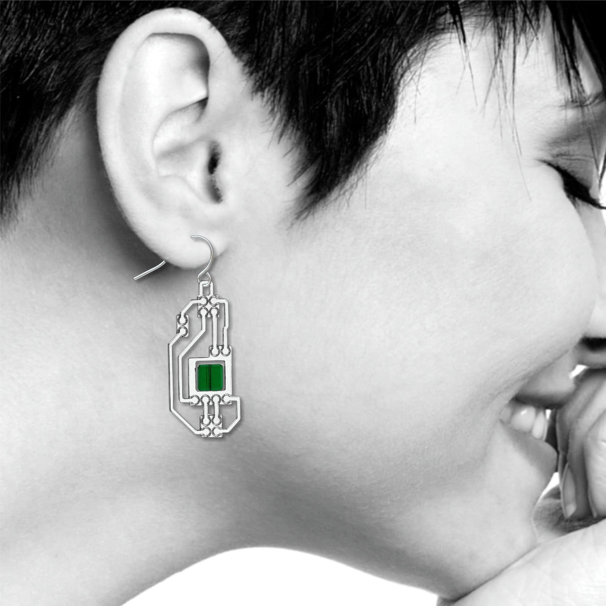 Circuits abstract silver drop earring worn on ear with intricate circuit board-inspired detailing and translucent green geometric accents in a modern industrial design