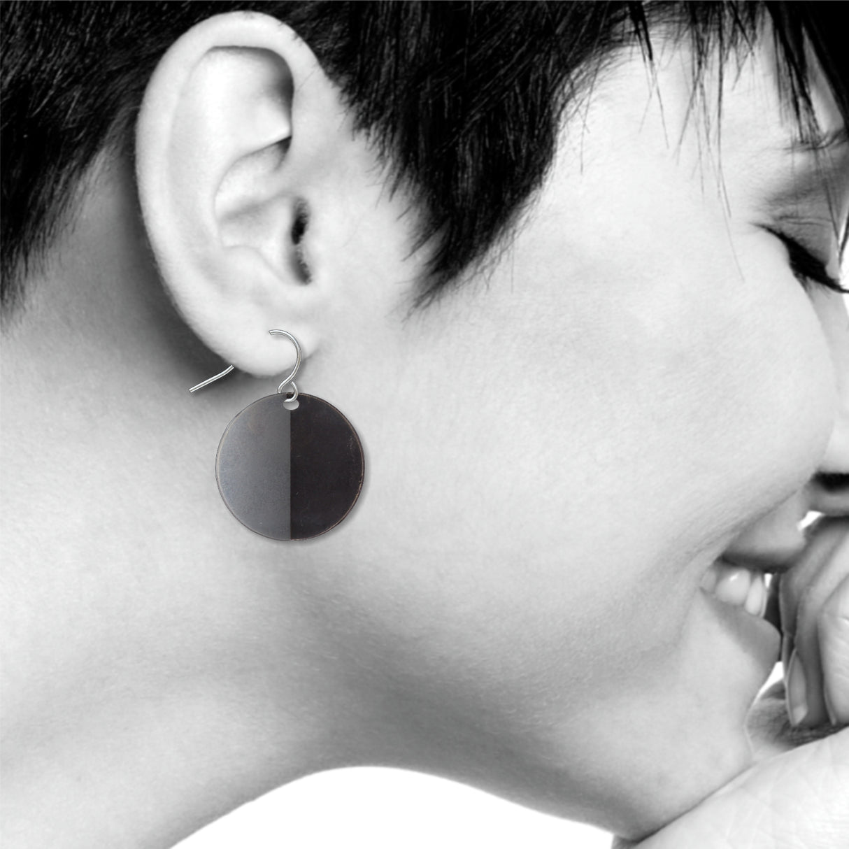 An Orb circular drop earring with a bold split-tone black and gray finish, shown worn on ear with a sleek minimalist modern art-inspired design