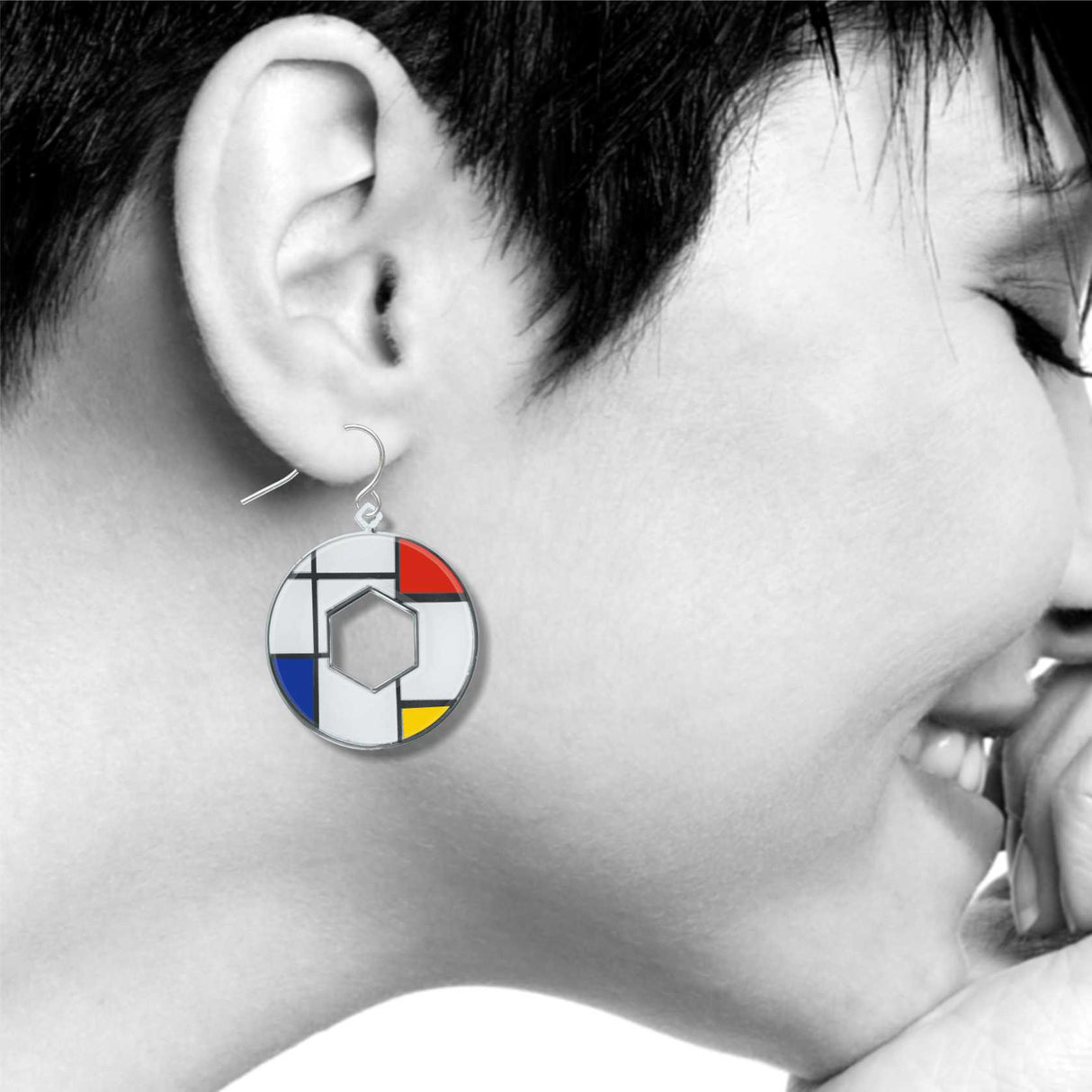 Model wearing a Utopia geometric dangle earring inspired by Mondrian artwork, featuring bold red, blue, yellow, black, and white enamel accents in a circular open-center design.