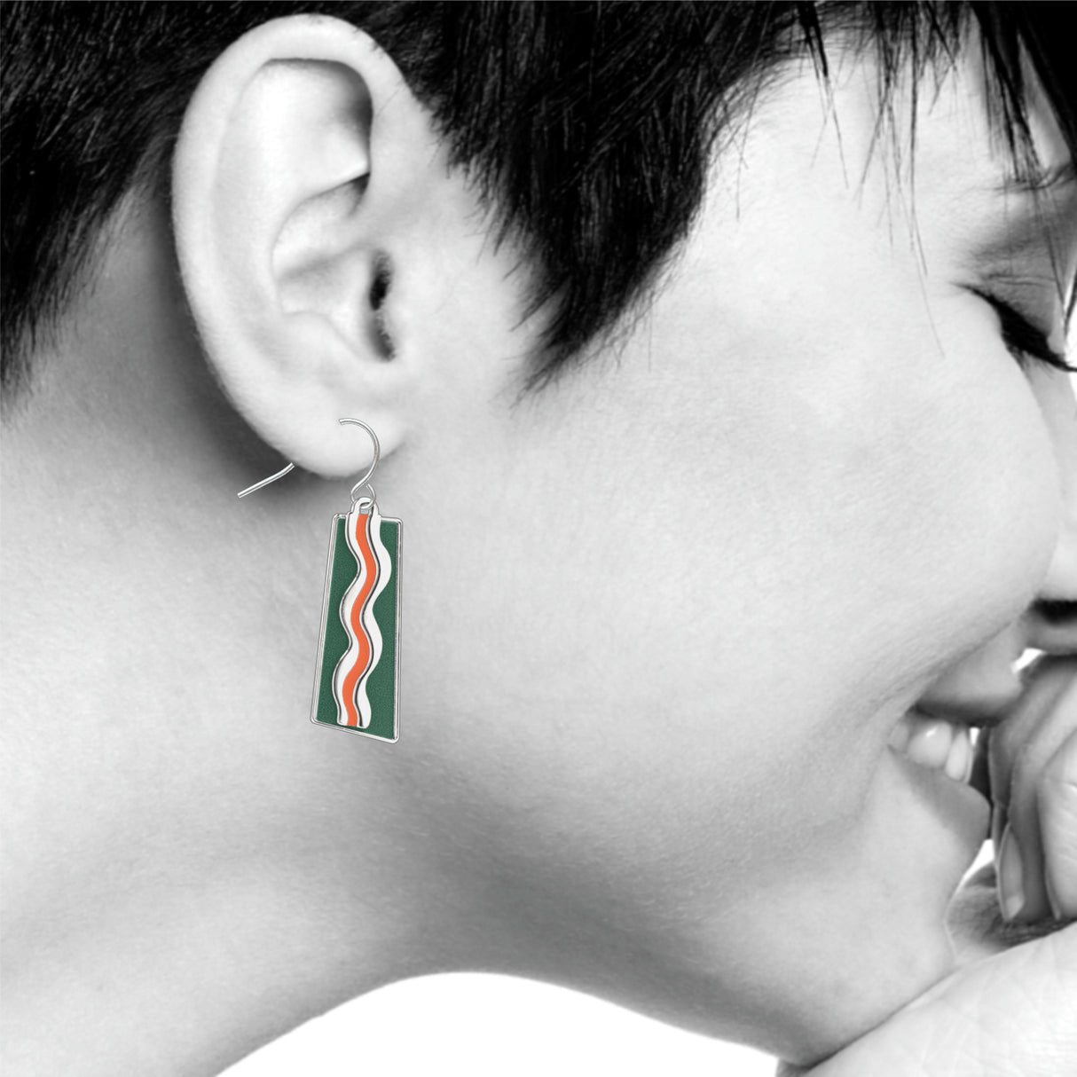 Model wearing a Matisse & the Fauves rectangular drop earring featuring flowing orange and white wave designs on a deep green enamel background inspired by Henri Matisse’s Fauvist color palette.