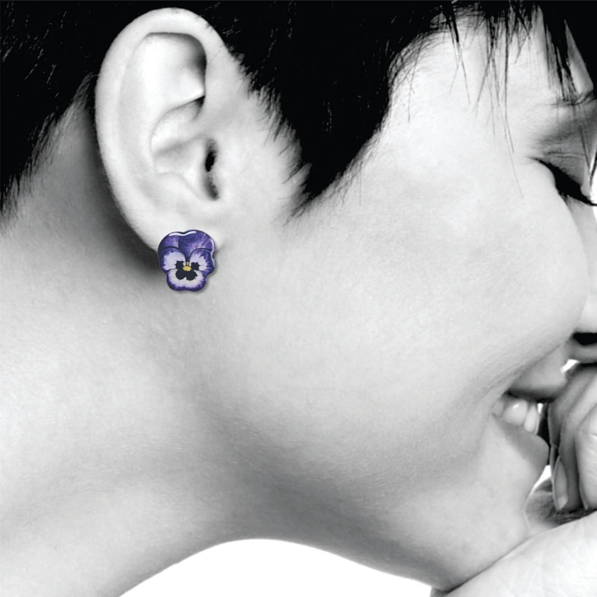 Close-up of a person wearing purple pansies flower earrings with a black and white background