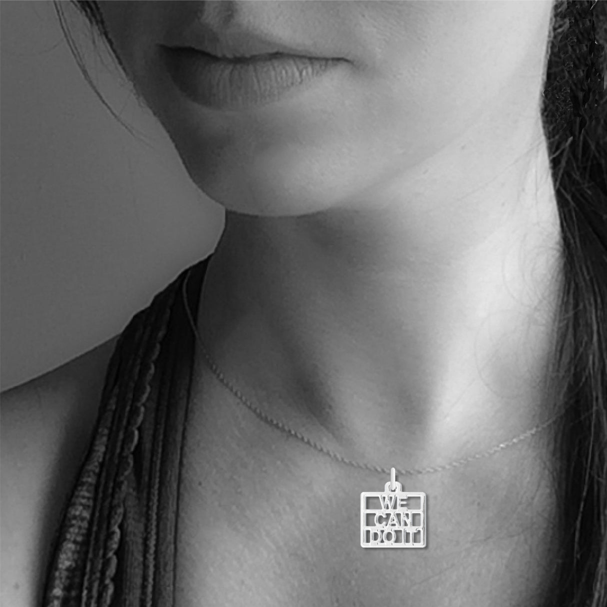 We Can Do It necklace shown worn on a model, featuring a silver-tone square pendant with cutout lettering on a delicate silver chain.
