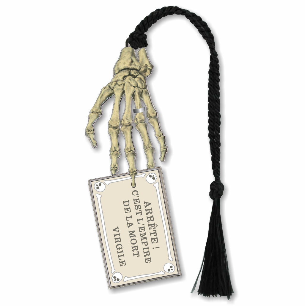 A metal bookmark in the shape of a skeleton hand with a attached card reading 'ARRET! CE LA VIVRE EST LA REINE DE LA MORT.' Adorned with a black braided tassel.