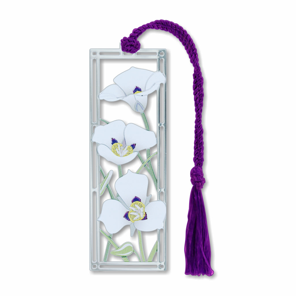 A metal bookmark featuring a detailed image of white to lavender-blue sego lily white petal flowers in a silver frame with a purple tassel.