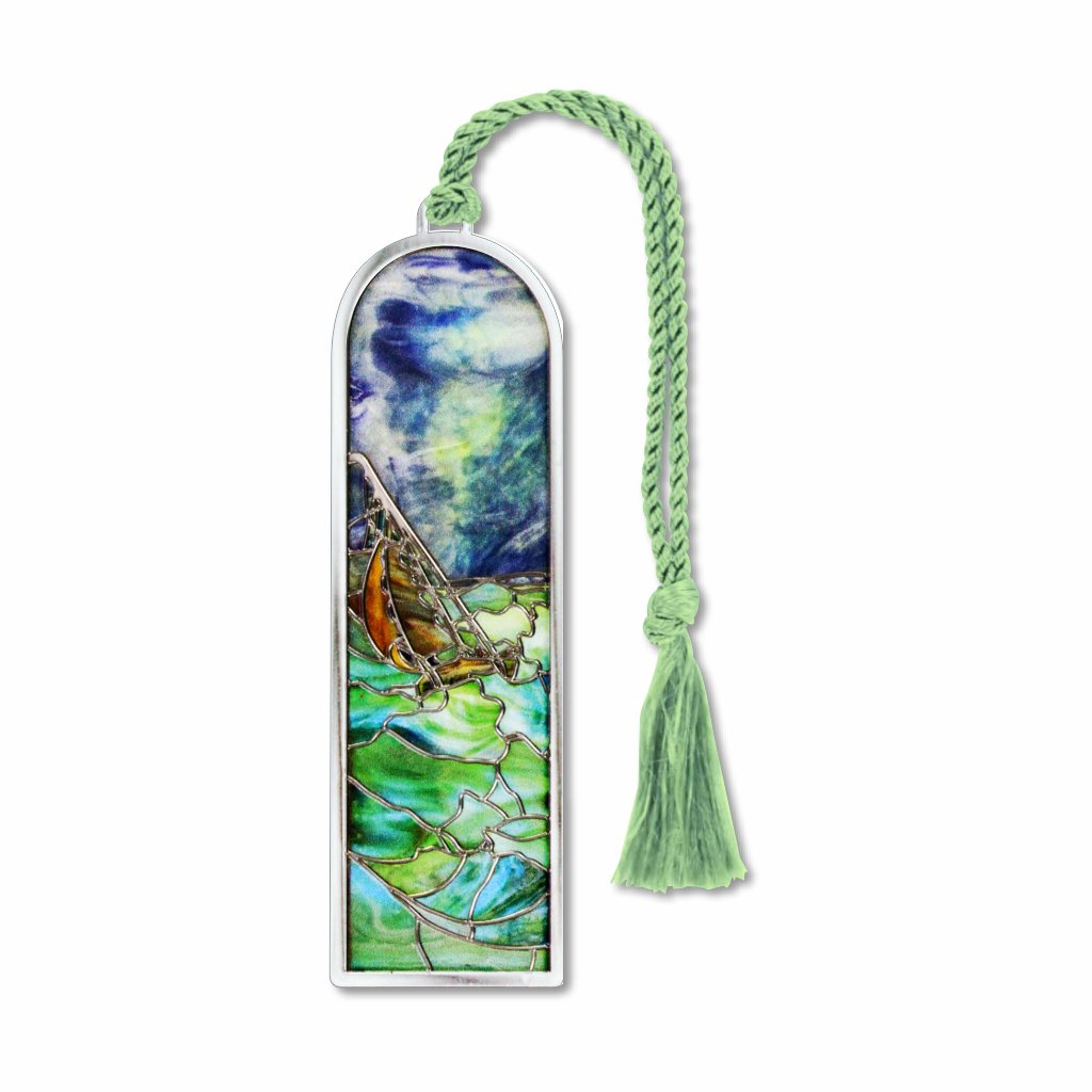 A silver metal Tiffany bookmark with a stained glass window design featuring a sailboat at sea with a stormy sky and sea foam green braided tassel.