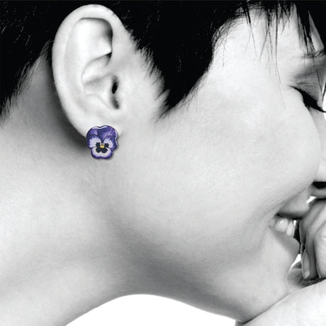 Close-up of a person wearing purple pansies flower earrings with a black and white background