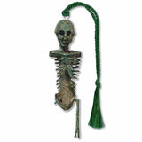A silver brass bookmark in the shape of a skeleton with one leg and no arms with a green tassel.